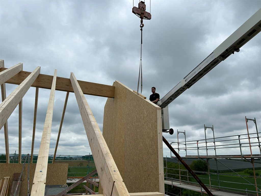 Teilansicht des Satteldaches mit Holzrahmenbauelementen, daneben ein Arbeiter auf einer Hebebühne.