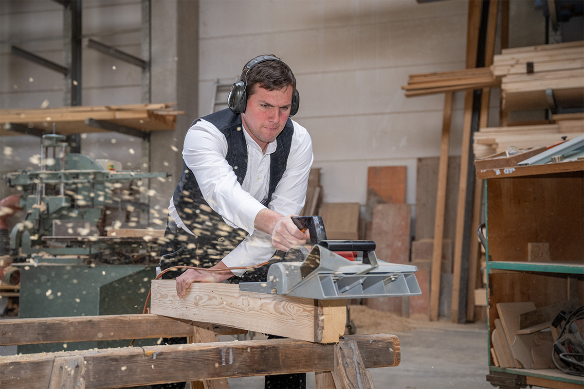Geschäftsführer Martin Frank bearbeitet in der Werkstatt einen Holzbalken mit einer elektrischen Holzsäge.