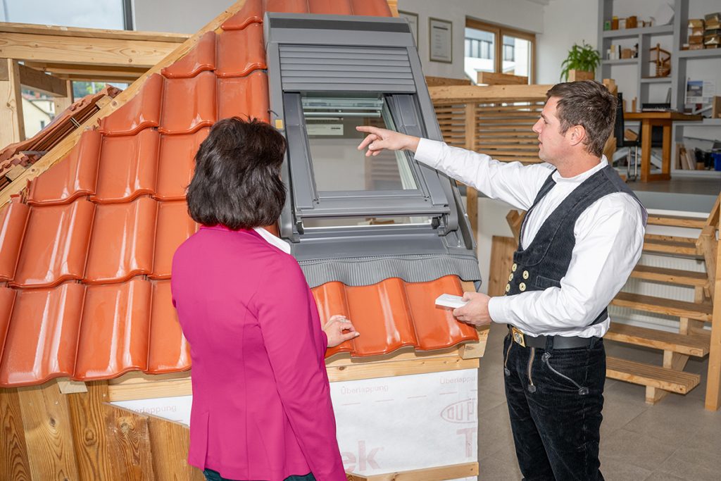 Geschäftsführer Martin Frank zeigt einer Frau im Ausstellungsraum der Firma ein Dachfenster als Anschauungsbeispiel.